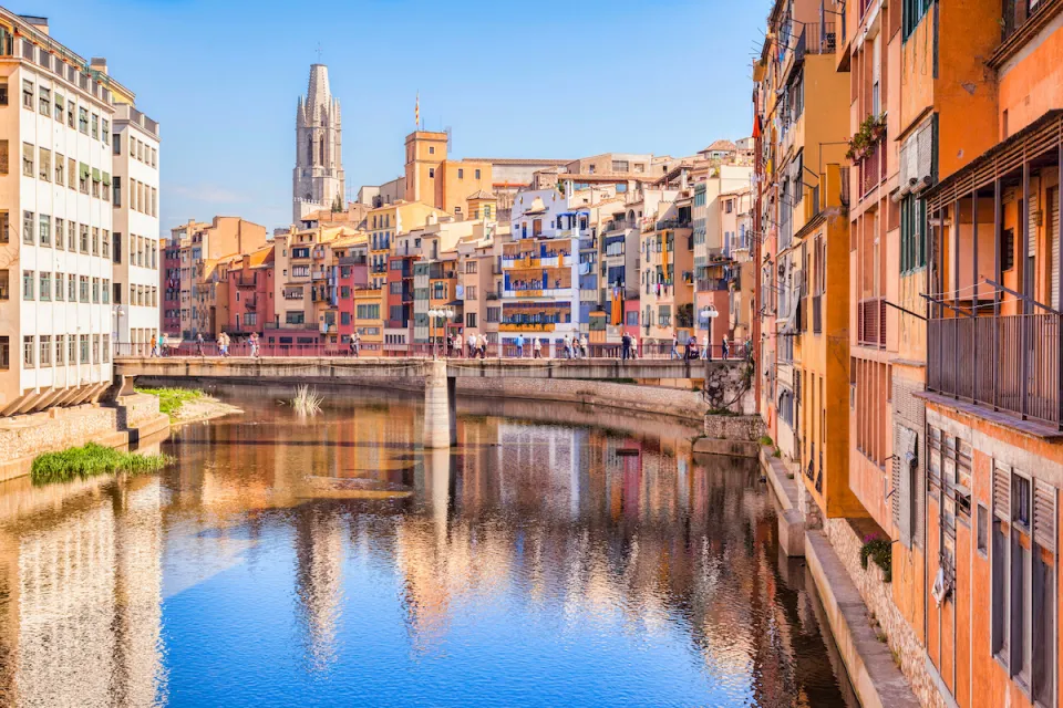 Old residential buildings along canal with ornate church in background in Girona, Catalonia, Spain.